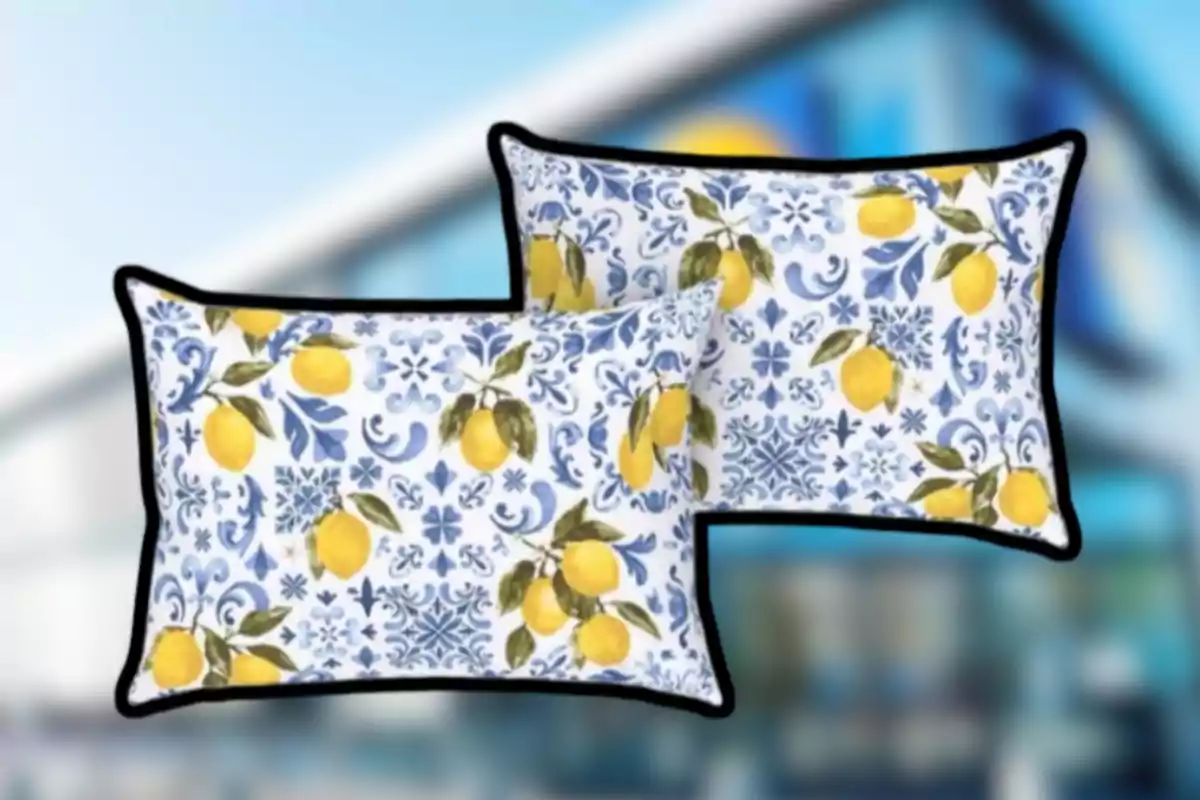 Dos cojines rectangulares con borde negro y estampado de limones amarillos y hojas verdes sobre un fondo blanco con patrones azules Dos cojines rectangulares con borde negro y estampado de limones amarillos y hojas verdes sobre un fondo blanco con patrones azules