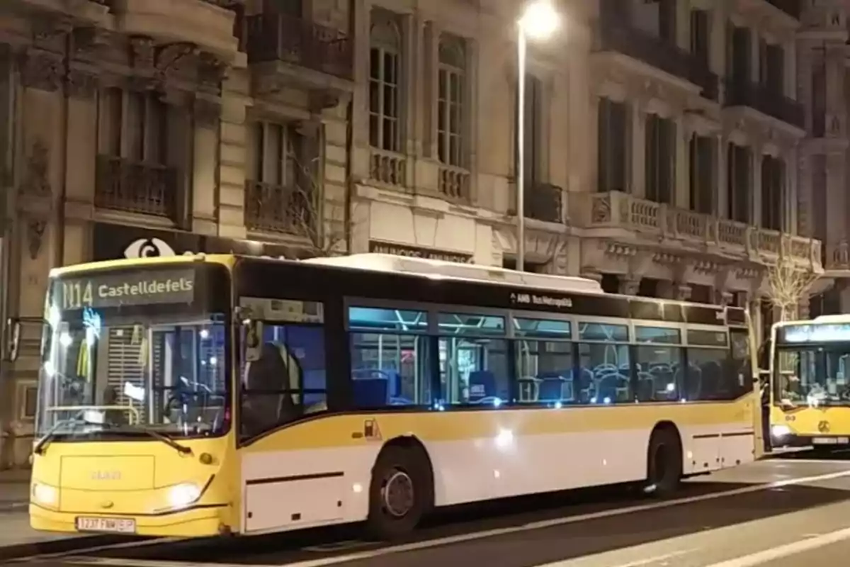 Autobús amarillo y blanco de la línea N14 estacionado en una calle urbana por la noche con edificios antiguos al fondo