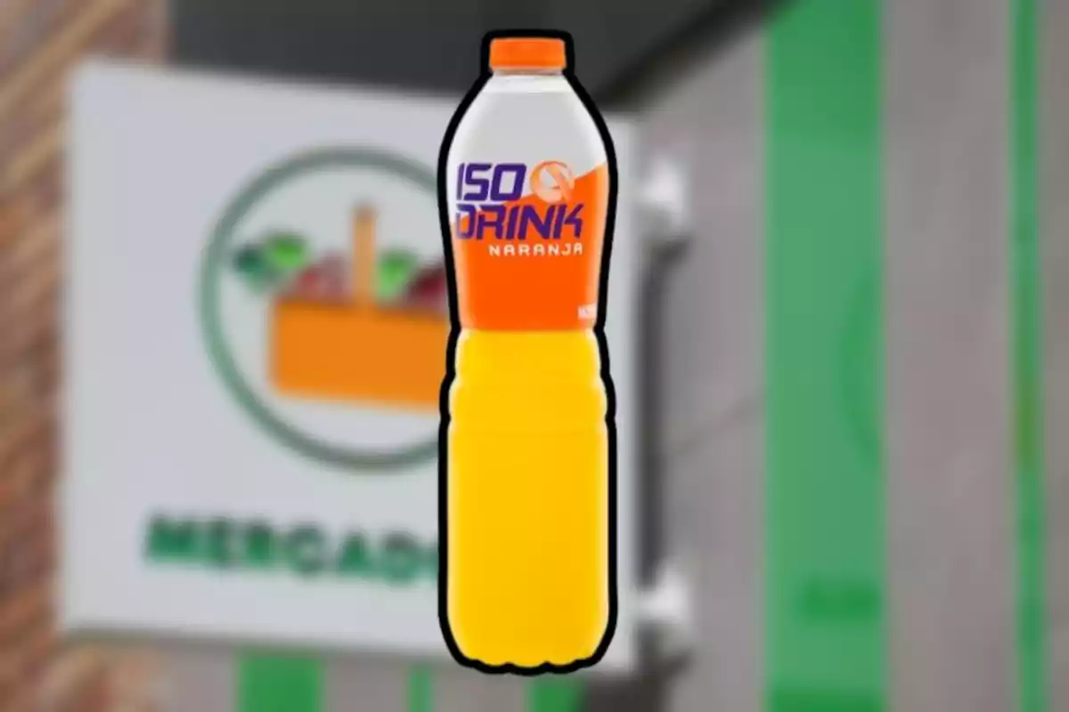 Botella de bebida isotónica sabor naranja con etiqueta naranja y blanca frente a un fondo borroso de supermercado Botella de bebida isotónica sabor naranja con etiqueta naranja y blanca frente a un fondo borroso de supermercado