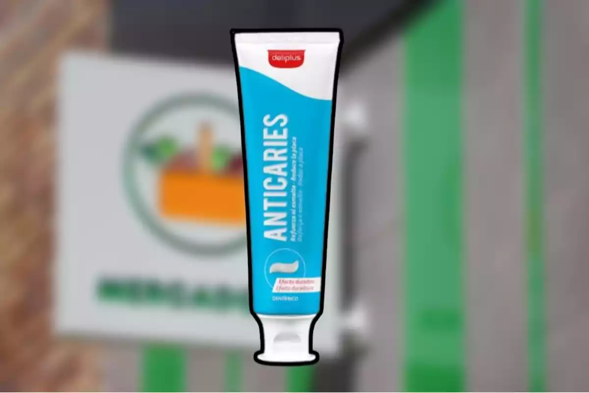 Pasta dental anticaries de la marca Deliplus frente a un cartel borroso de supermercado Pasta dental anticaries de la marca Deliplus frente a un cartel borroso de supermercado