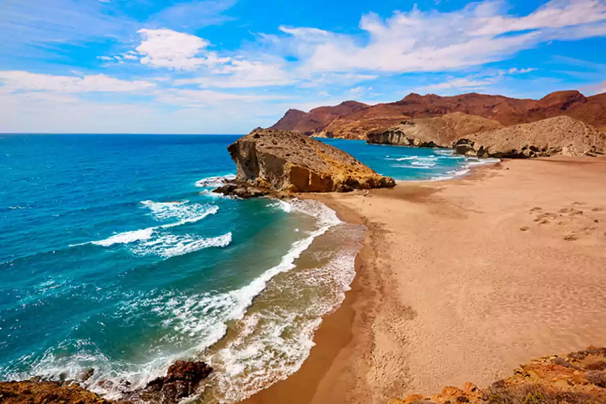 Playa de arena dorada con aguas turquesas y formaciones rocosas bajo un cielo azul con algunas nubes Playa de arena dorada con aguas turquesas y formaciones rocosas bajo un cielo azul con algunas nubes