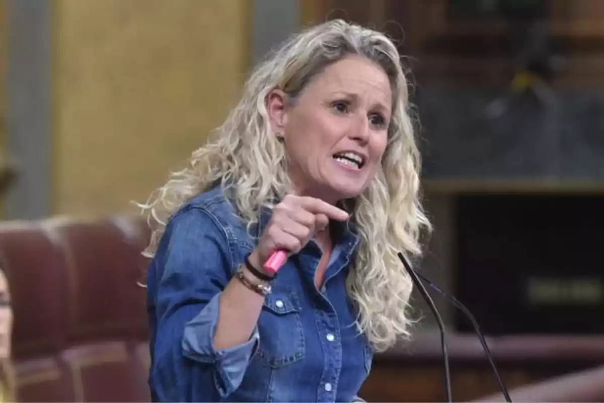 Mujer de cabello rubio rizado hablando apasionadamente y gesticulando con la mano en un recinto parlamentario Mujer de cabello rubio rizado hablando apasionadamente y gesticulando con la mano en un recinto parlamentario