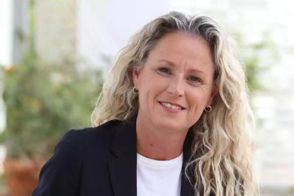 Mujer de cabello rubio rizado y largo con chaqueta oscura y camiseta blanca sonriendo al aire libre Mujer de cabello rubio rizado y largo con chaqueta oscura y camiseta blanca sonriendo al aire libre