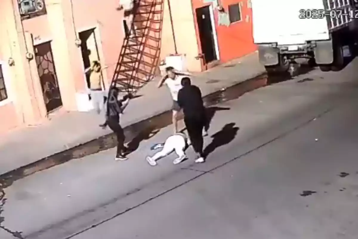 Varias personas están en una calle, una de ellas está tirada en el suelo mientras otras dos parecen discutir y una más baja por una escalera metálica junto a un edificio. Varias personas están en una calle, una de ellas está tirada en el suelo mientras otras dos parecen discutir y una más baja por una escalera metálica junto a un edificio.