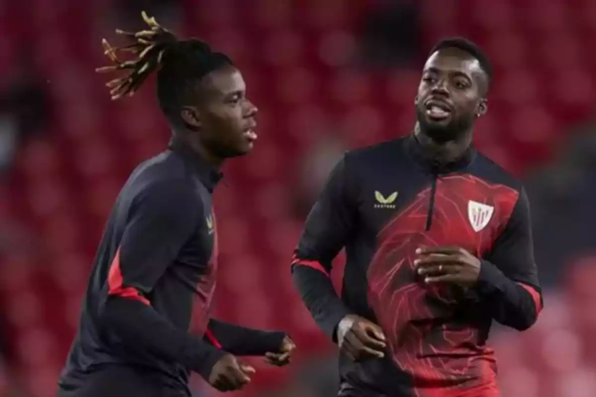 Dos futbolistas del Athletic Club entrenando en el campo con uniforme negro y rojo