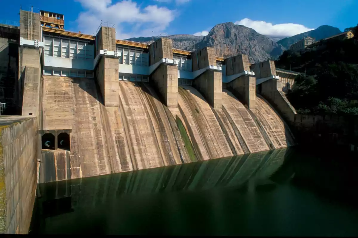 Presa de concreto con compuertas y agua acumulada al pie de una montaña bajo un cielo azul Presa de concreto con compuertas y agua acumulada al pie de una montaña bajo un cielo azul