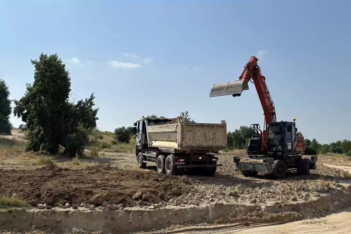 Excavadora cargando tierra en la caja de un camión en una zona de obras al aire libre