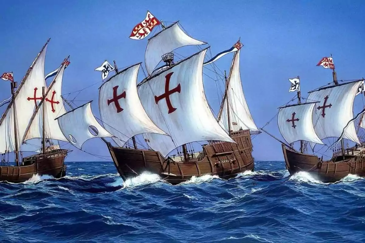 Tres carabelas antiguas navegan juntas sobre un mar azul con velas blancas decoradas con cruces rojas