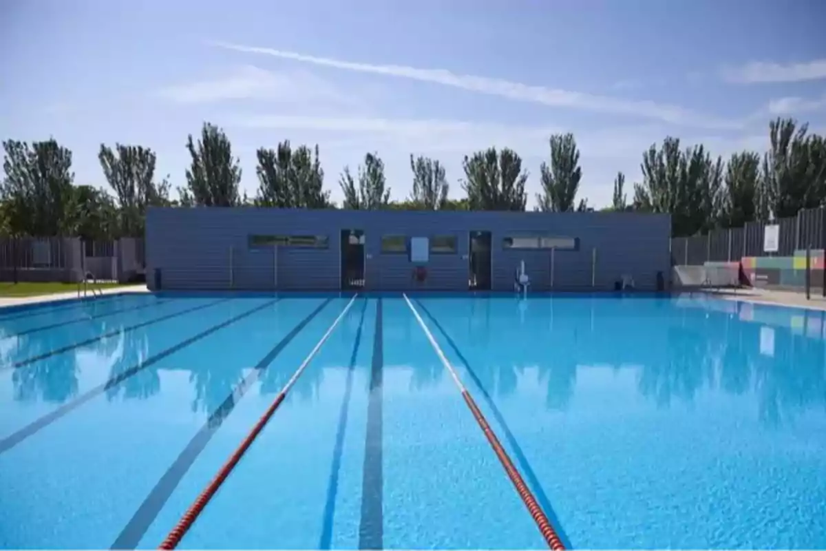 Piscina olímpica al aire libre con carriles de natación y un edificio al fondo en un día soleado