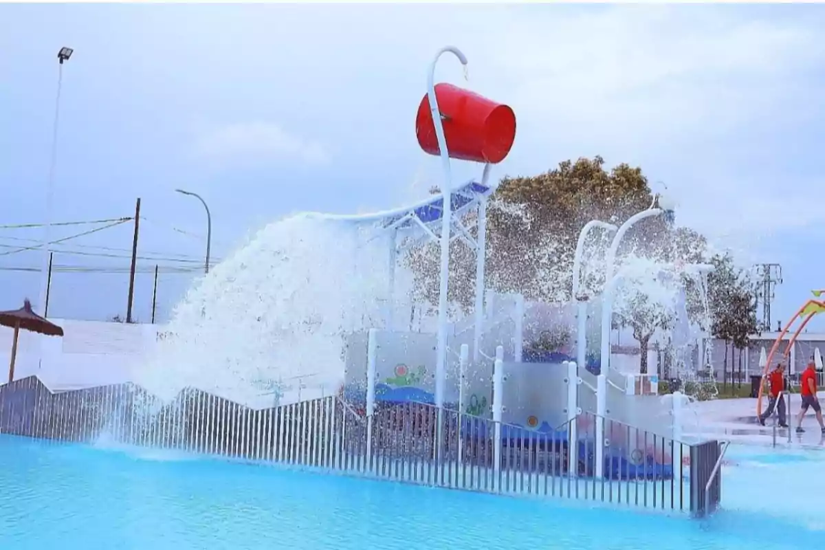 Parque acuático con un gran cubo rojo volcando agua sobre una estructura de juegos infantiles en una piscina Parque acuático con un gran cubo rojo volcando agua sobre una estructura de juegos infantiles en una piscina