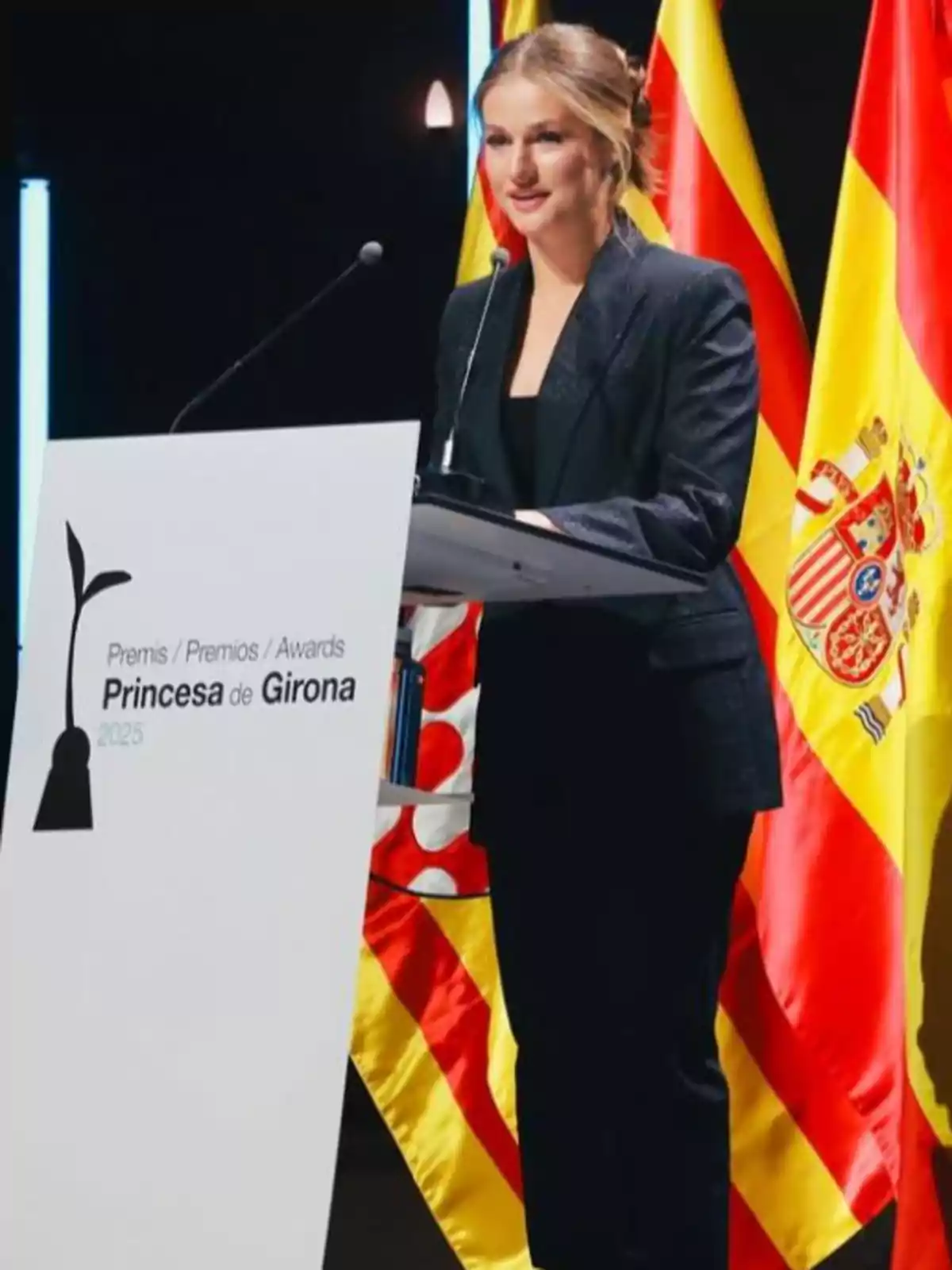 La princesa Leonor con traje oscuro hablando en un podio durante los Premios Princesa de Girona 2025 con banderas de España y Cataluña al fondo La princesa Leonor con traje oscuro hablando en un podio durante los Premios Princesa de Girona 2025 con banderas de España y Cataluña al fondo