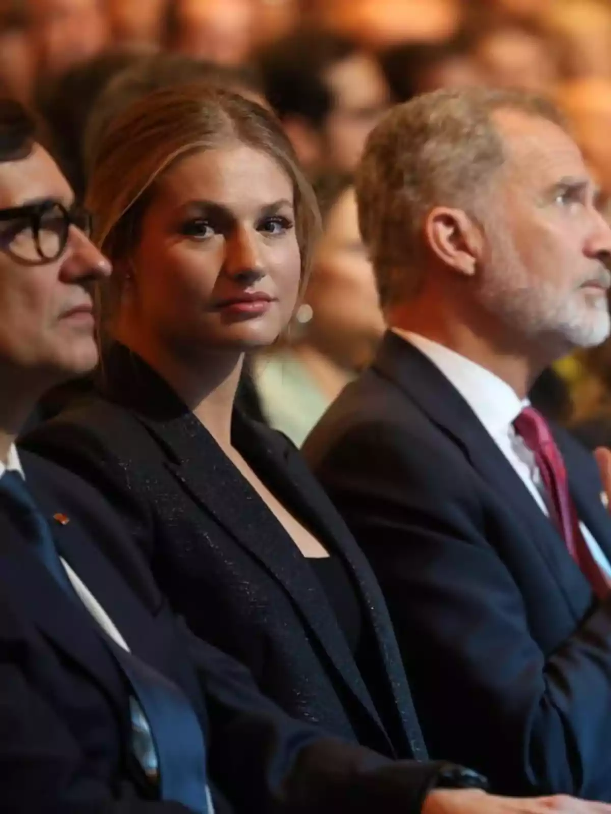 Salvador Illa, la princesa Leonor y Felipe VI sentadas en un evento formal con la mujer en el centro mirando hacia la cámara y los hombres a los lados mirando al frente