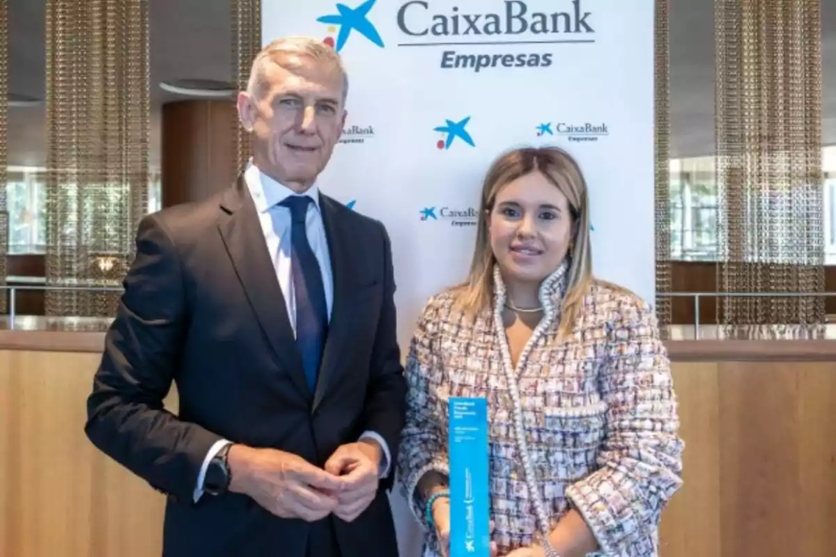 Dos personas posan frente a un cartel de CaixaBank Empresas, una de ellas sostiene un trofeo azul Dos personas posan frente a un cartel de CaixaBank Empresas, una de ellas sostiene un trofeo azul