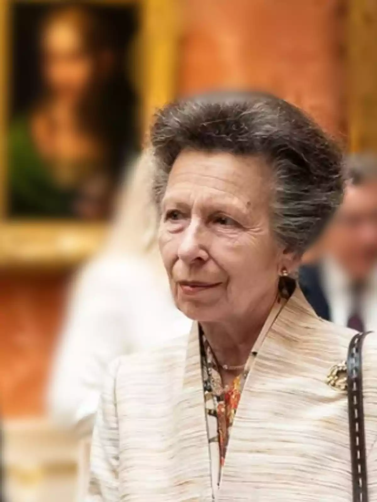 Mujer mayor de cabello canoso y peinado voluminoso, vestida elegantemente con un broche dorado, en una galería de arte con un cuadro desenfocado al fondo Mujer mayor de cabello canoso y peinado voluminoso, vestida elegantemente con un broche dorado, en una galería de arte con un cuadro desenfocado al fondo