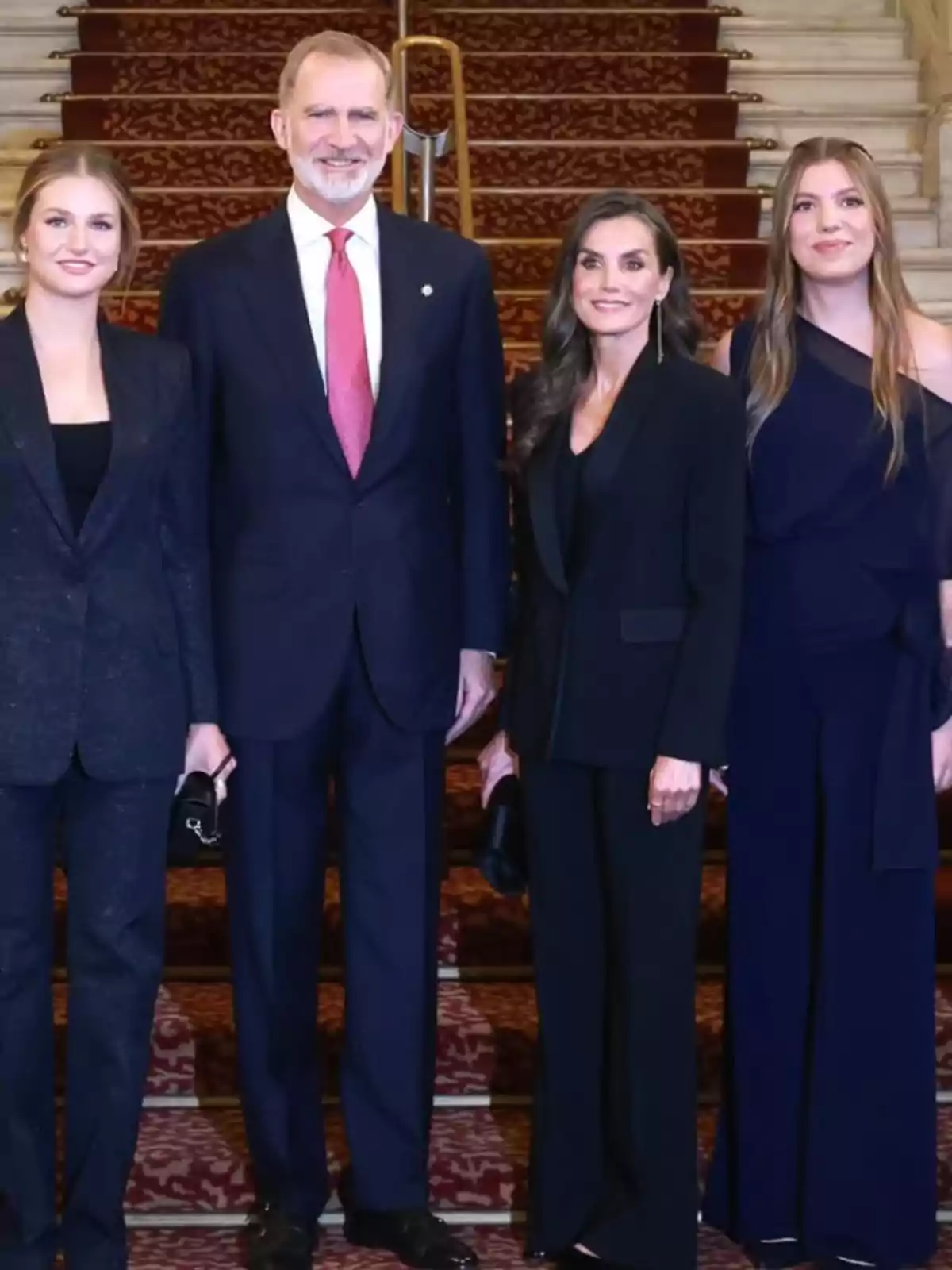 Four elegantly dressed people pose together on a carpeted staircase. Four elegantly dressed people pose together on a carpeted staircase.