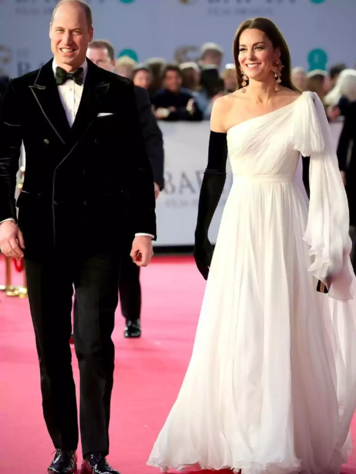 Elegantly dressed couple walking on a red carpet, he in a black tuxedo and she in a one-shoulder white dress with long black gloves Elegantly dressed couple walking on a red carpet, he in a black tuxedo and she in a one-shoulder white dress with long black gloves