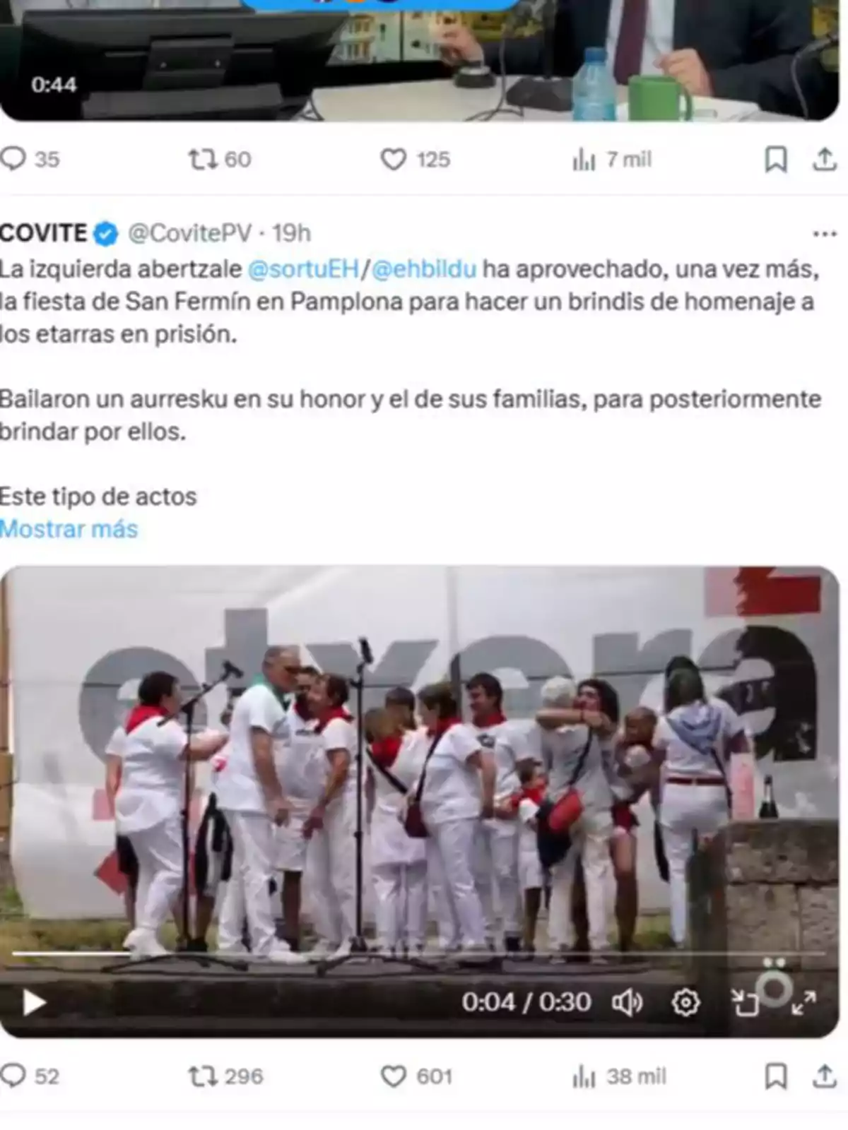 Grupo de personas vestidas de blanco con pañuelos rojos reunidas en un escenario al aire libre frente a micrófonos durante una celebración Grupo de personas vestidas de blanco con pañuelos rojos reunidas en un escenario al aire libre frente a micrófonos durante una celebración