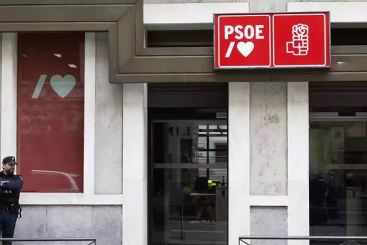 Fachada de un edificio con un letrero rojo del PSOE y un policía de pie en la entrada Fachada de un edificio con un letrero rojo del PSOE y un policía de pie en la entrada