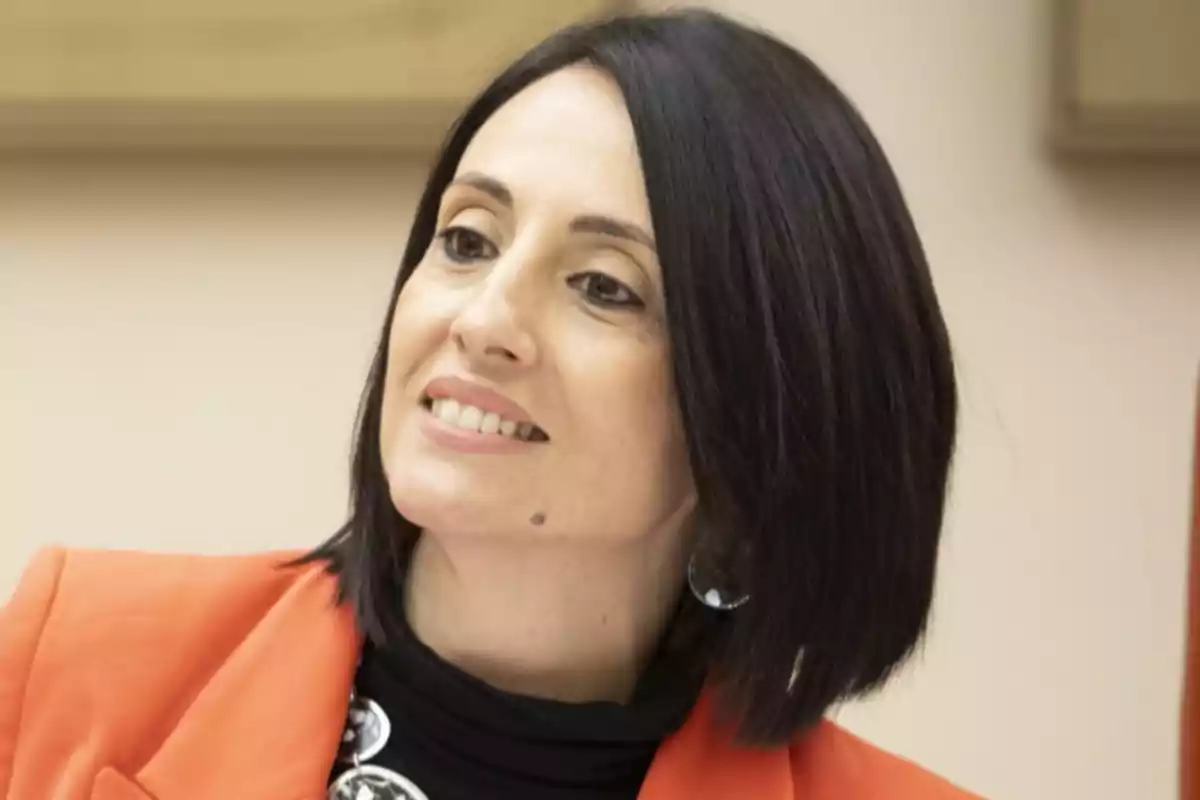 Mujer de cabello oscuro y liso con chaqueta naranja y expresión sonriente Mujer de cabello oscuro y liso con chaqueta naranja y expresión sonriente