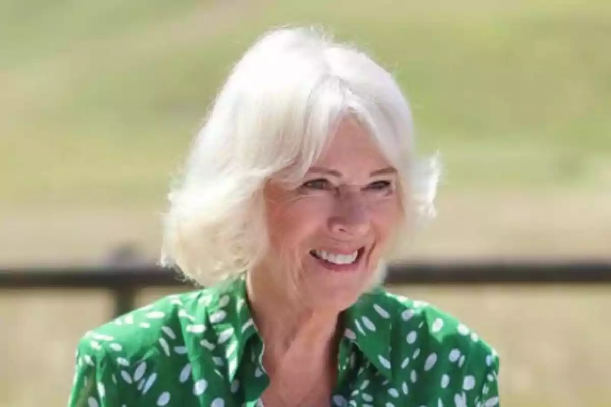 Close-up of Queen Camilla smiling while wearing a green blouse with white polka dots in a blurred outdoor setting. Close-up of Queen Camilla smiling while wearing a green blouse with white polka dots in a blurred outdoor setting.