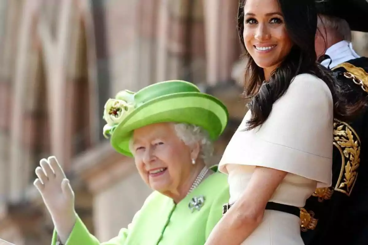 Dos mujeres sonríen en un evento formal una de ellas lleva un conjunto verde con sombrero a juego y la otra viste de blanco Dos mujeres sonríen en un evento formal una de ellas lleva un conjunto verde con sombrero a juego y la otra viste de blanco