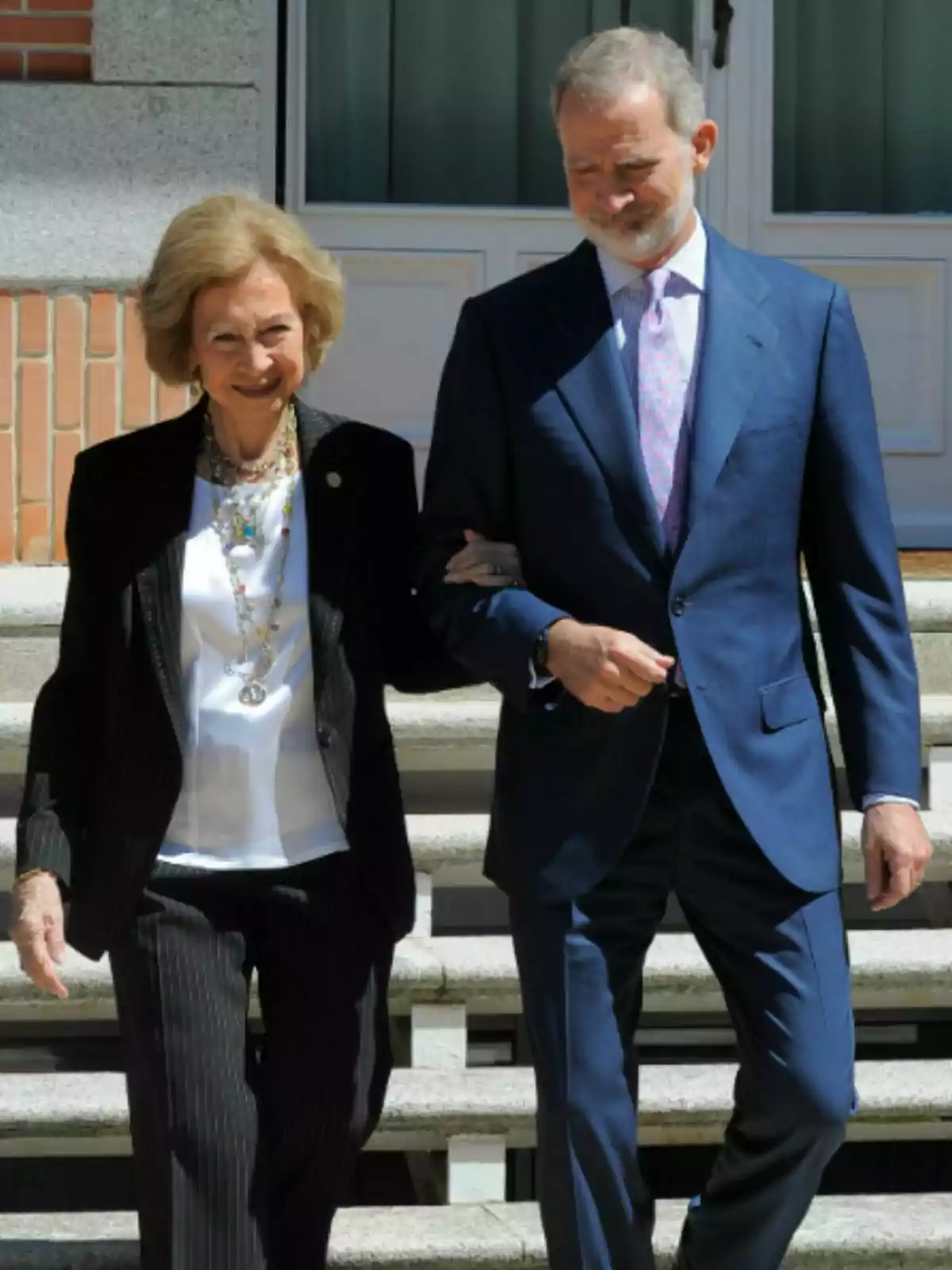 La reina Sofía y Felipe VI elegantemente vestidos caminan juntos del brazo bajando unas escaleras al aire libre La reina Sofía y Felipe VI elegantemente vestidos caminan juntos del brazo bajando unas escaleras al aire libre