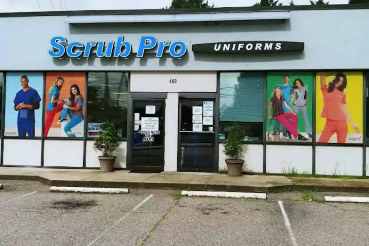 Storefront of a shop called Scrub Pro Uniforms with posters of people wearing medical uniforms in the windows and two flowerpots next to the entrance. Storefront of a shop called Scrub Pro Uniforms with posters of people wearing medical uniforms in the windows and two flowerpots next to the entrance.
