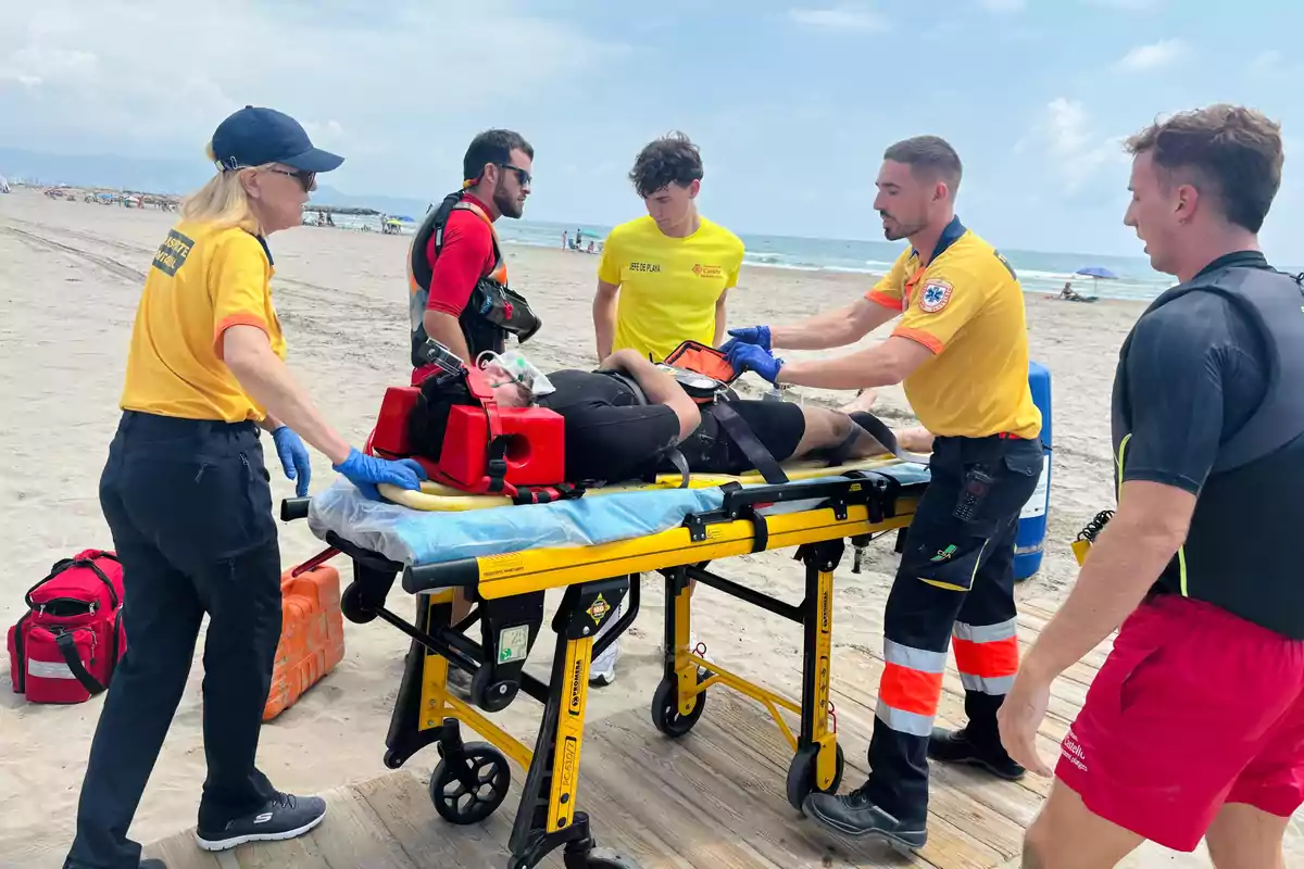 Equipo de socorristas y paramédicos atiende a una persona herida en una camilla sobre la playa mientras la trasladan para recibir atención médica