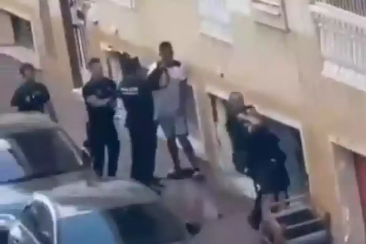 Varios policías rodean a un hombre en una calle junto a un edificio y un coche estacionado. Varios policías rodean a un hombre en una calle junto a un edificio y un coche estacionado.