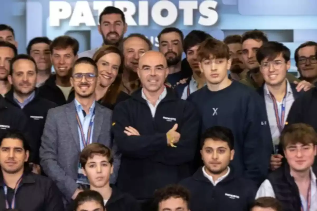 Grupo de personas posando juntas y sonriendo frente a un cartel que dice Patriots Grupo de personas posando juntas y sonriendo frente a un cartel que dice Patriots