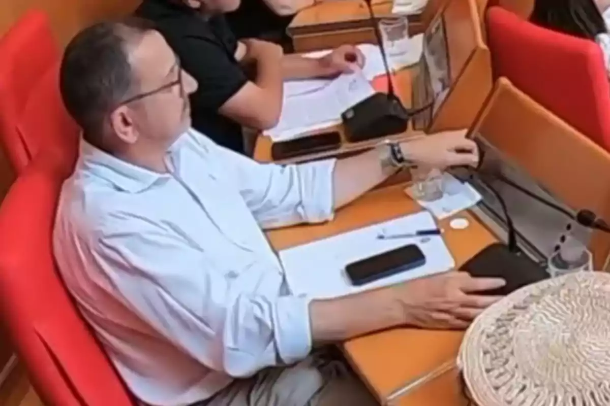 Hombre sentado en una silla roja en una sala de reuniones con papeles, un bolígrafo y un teléfono móvil sobre la mesa Hombre sentado en una silla roja en una sala de reuniones con papeles, un bolígrafo y un teléfono móvil sobre la mesa