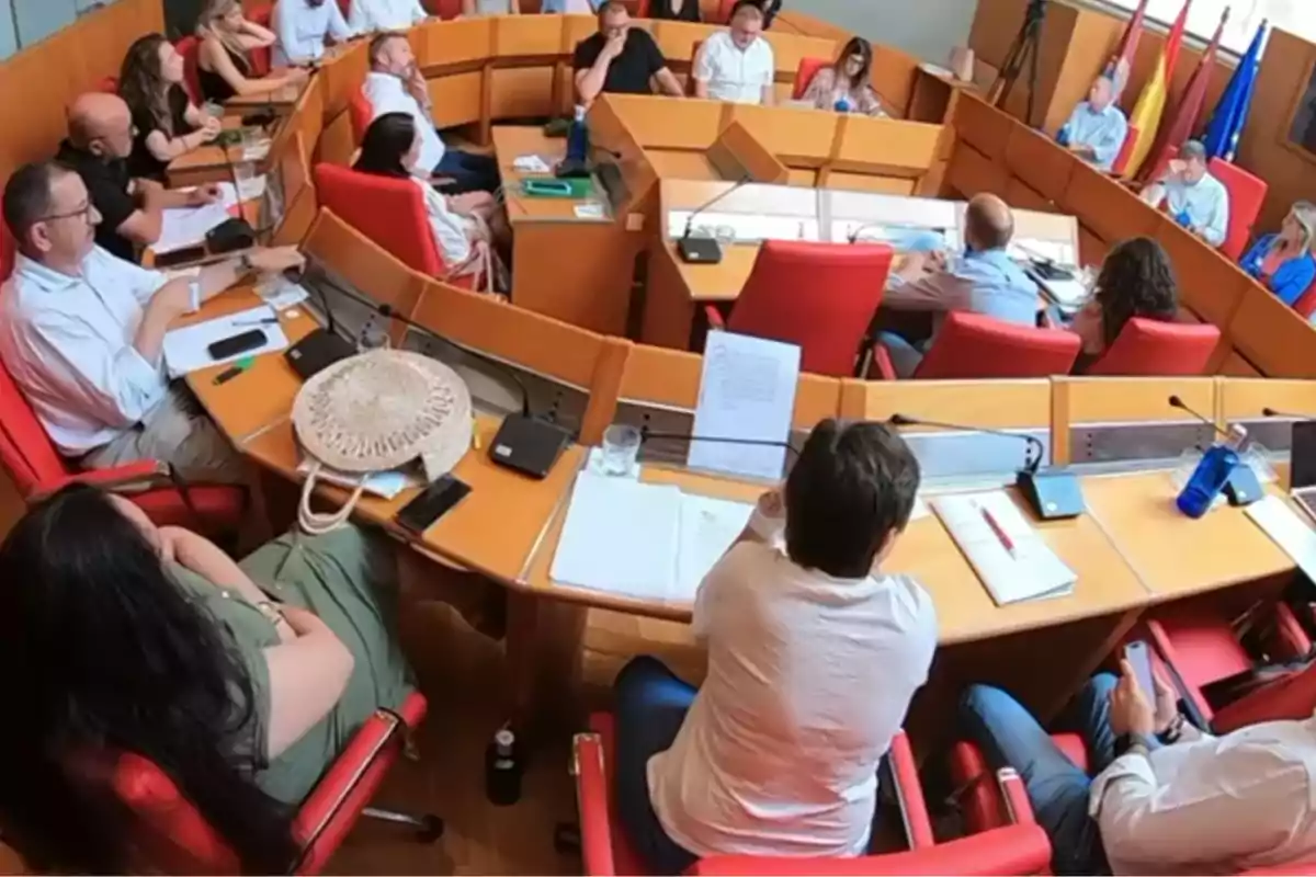 Personas sentadas alrededor de una mesa en una sala de reuniones con documentos y dispositivos electrónicos sobre la mesa Personas sentadas alrededor de una mesa en una sala de reuniones con documentos y dispositivos electrónicos sobre la mesa