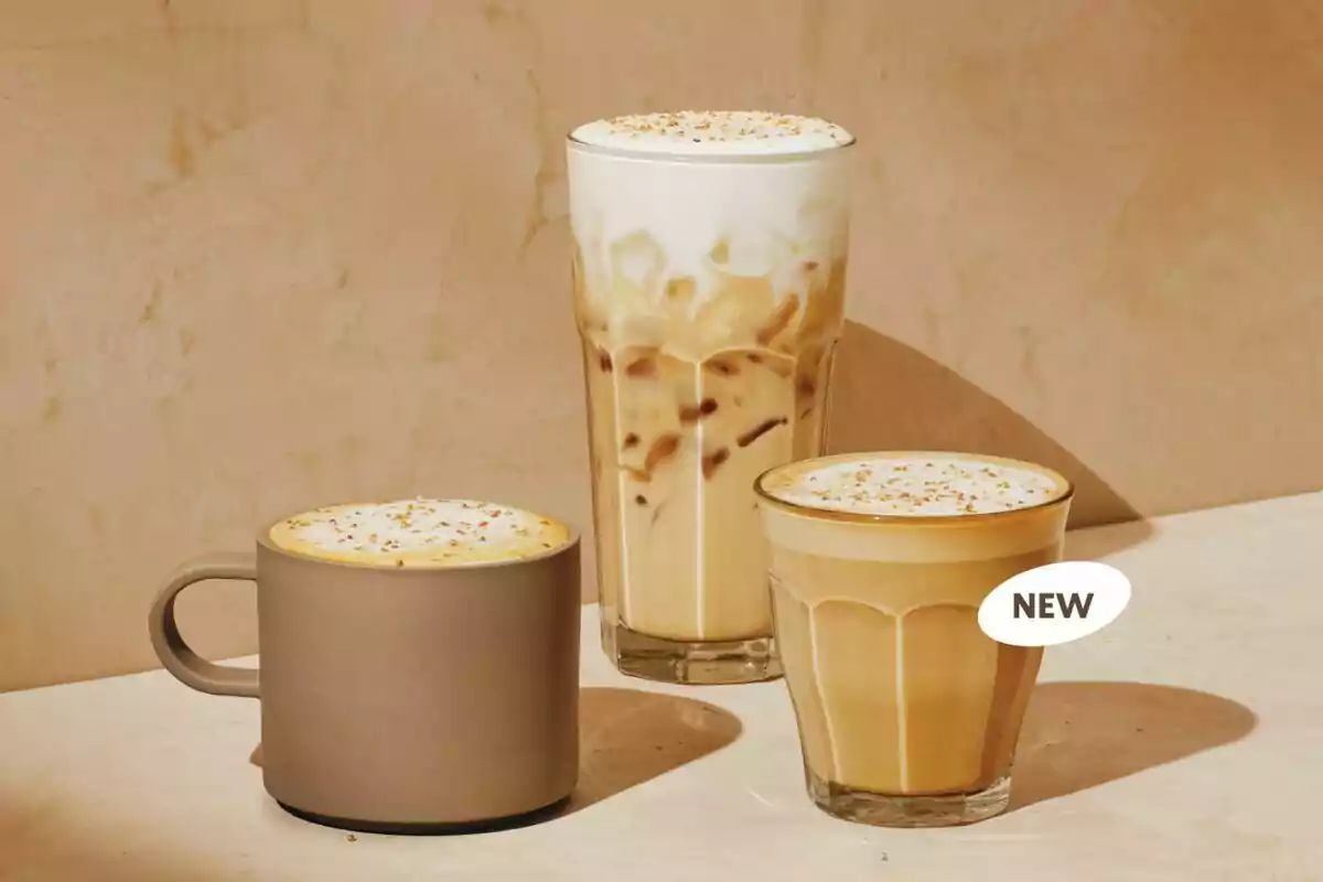 Tres bebidas de café con espuma y decorado en la parte superior, servidas en diferentes vasos y una taza sobre una superficie clara con fondo beige Tres bebidas de café con espuma y decorado en la parte superior, servidas en diferentes vasos y una taza sobre una superficie clara con fondo beige