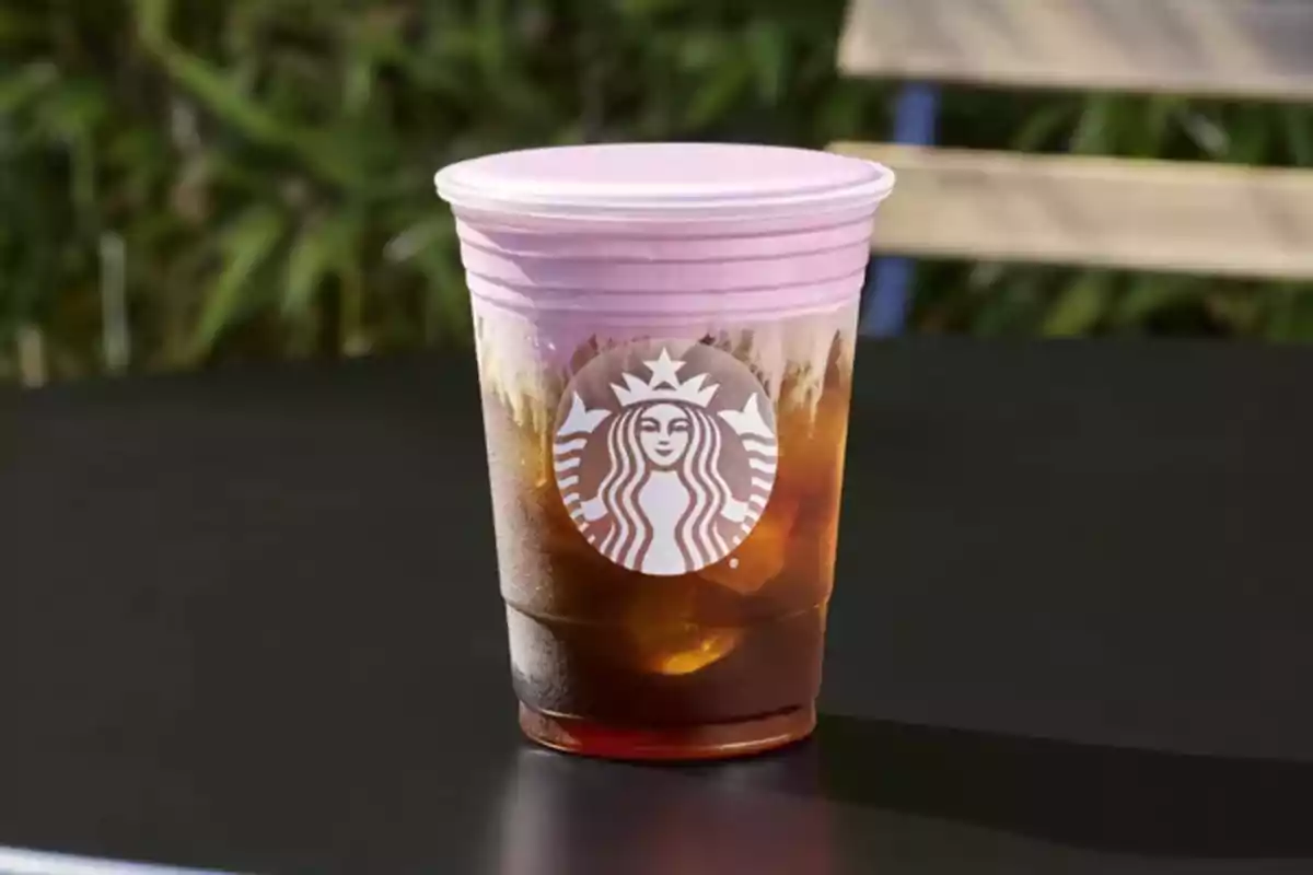 Starbucks plastic cup with a cold drink and a pink lid on a black outdoor table Starbucks plastic cup with a cold drink and a pink lid on a black outdoor table