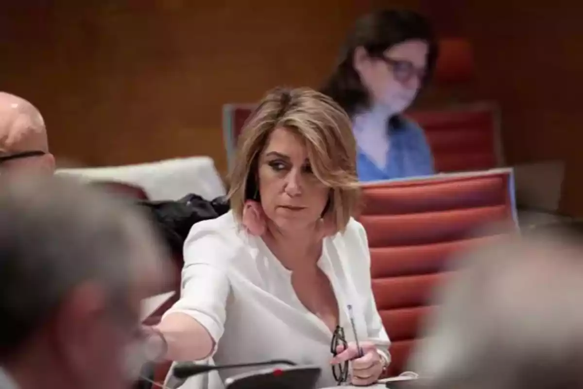 Mujer de cabello rubio y corto sentada en una sala de reuniones con expresión seria mientras sostiene unas gafas y un bolígrafo Mujer de cabello rubio y corto sentada en una sala de reuniones con expresión seria mientras sostiene unas gafas y un bolígrafo
