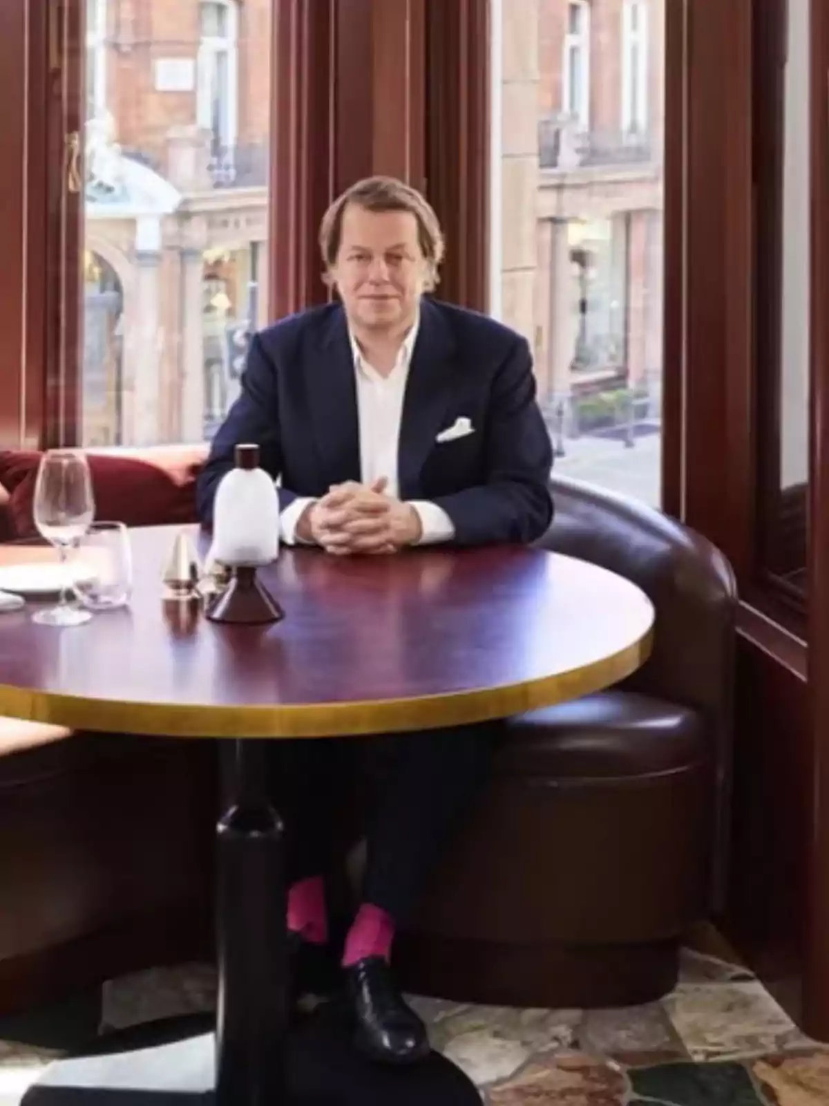 Hombre de traje azul marino sentado solo en una mesa redonda de un restaurante elegante con ventanas grandes y luz natural Hombre de traje azul marino sentado solo en una mesa redonda de un restaurante elegante con ventanas grandes y luz natural