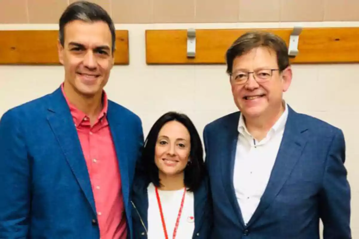 Tres personas posan sonrientes frente a una pared blanca con percheros de madera Tres personas posan sonrientes frente a una pared blanca con percheros de madera