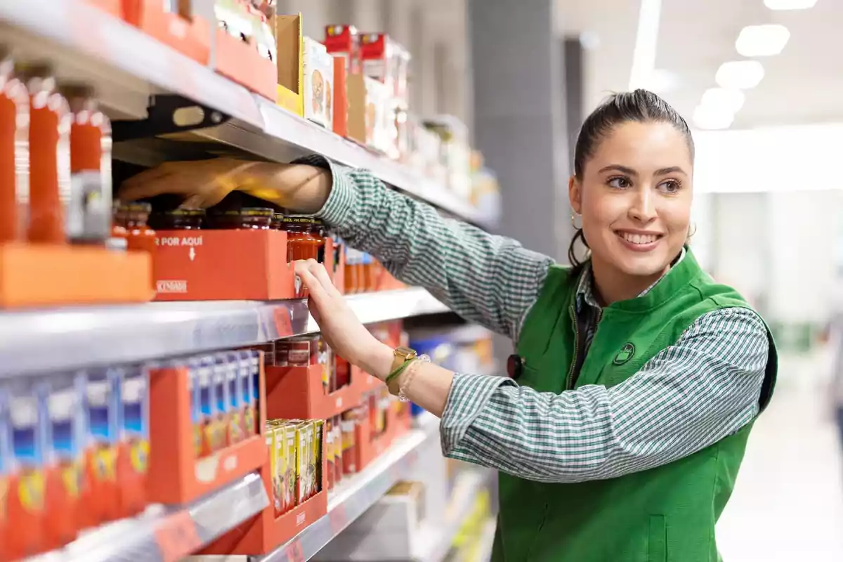 Empleada de supermercado acomodando productos en un estante y sonriendo