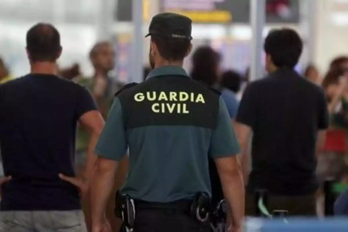 Un agente de la Guardia Civil de espaldas en un lugar concurrido con varias personas alrededor.