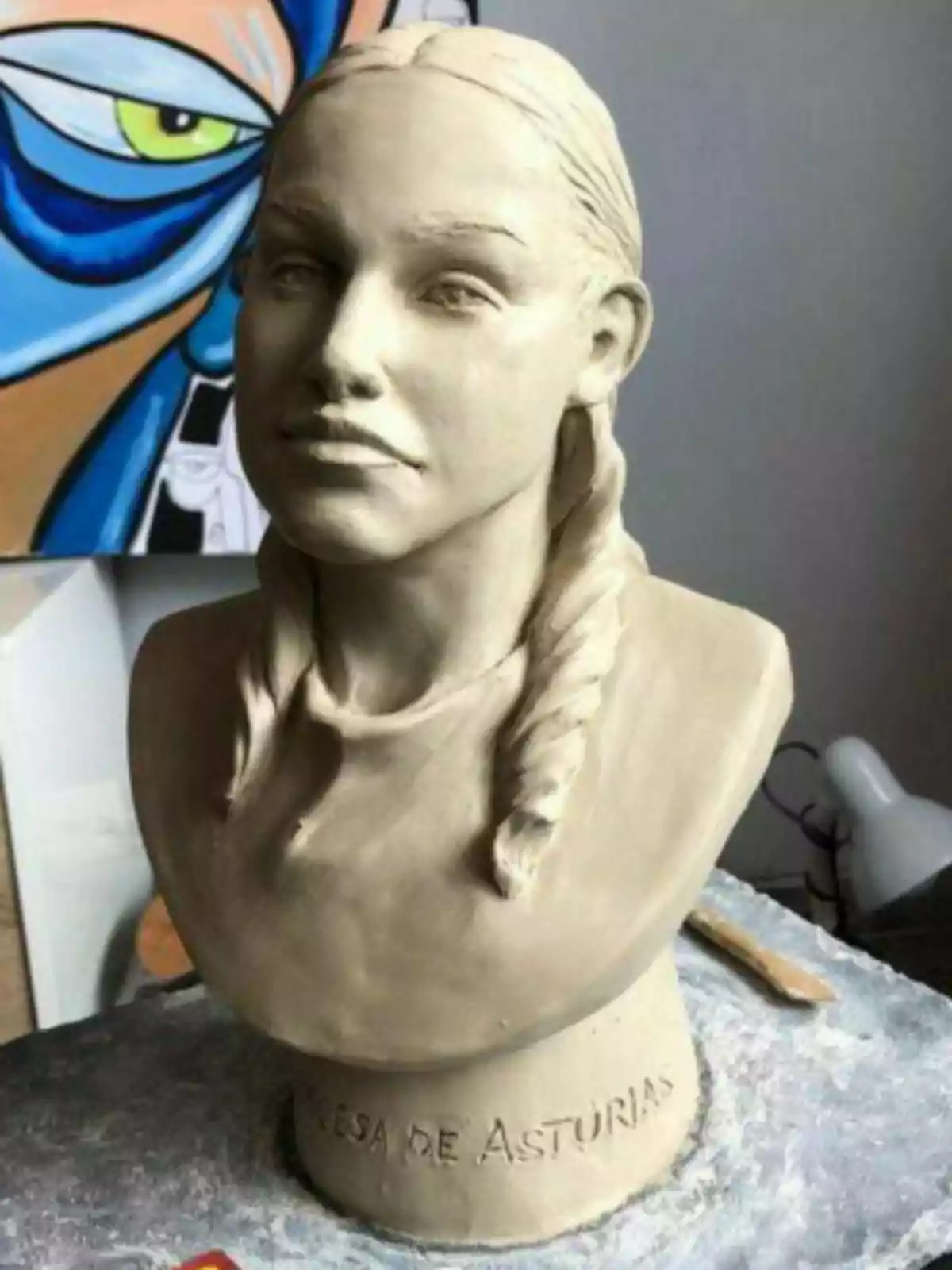 Bust of Princess Leonor with a braid made of clay on a work table with a colorful painting in the background. Bust of Princess Leonor with a braid made of clay on a work table with a colorful painting in the background.