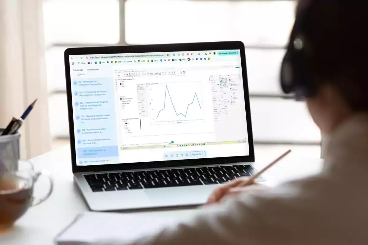 Persona estudiando frente a una laptop que muestra una gráfica en la pantalla mientras toma notas en una libreta