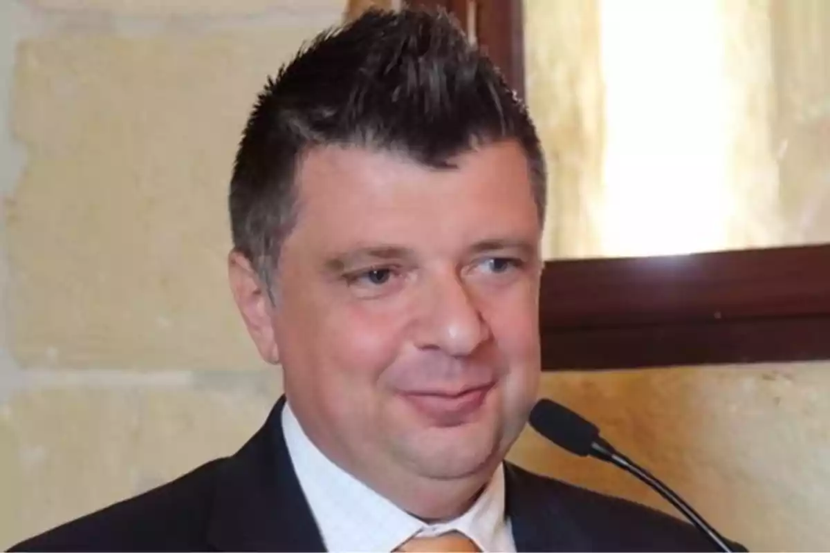 Hombre de cabello corto y oscuro usando traje y corbata naranja hablando frente a un micrófono Hombre de cabello corto y oscuro usando traje y corbata naranja hablando frente a un micrófono