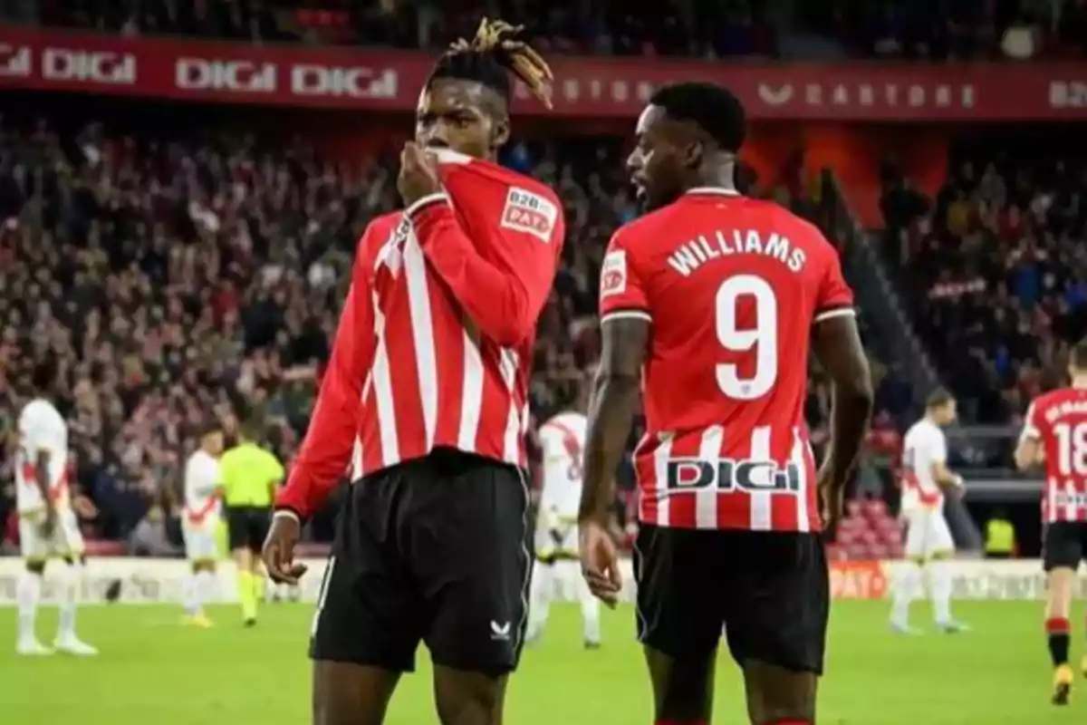 Dos futbolistas con uniforme rojo y blanco celebran en un estadio lleno de espectadores uno de ellos sostiene su camiseta mientras el otro muestra el número 9 y el nombre Williams en la espalda Dos futbolistas con uniforme rojo y blanco celebran en un estadio lleno de espectadores uno de ellos sostiene su camiseta mientras el otro muestra el número 9 y el nombre Williams en la espalda