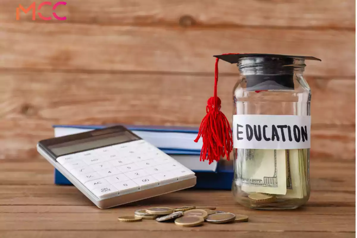 Frasco con dinero etiquetado como educación junto a una calculadora, monedas y libros sobre una mesa de madera