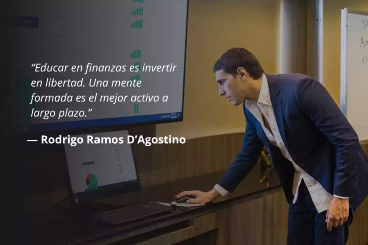 Hombre de traje azul interactuando con una computadora mientras observa una pantalla grande con gráficos y una cita sobre educación financiera escrita en la imagen