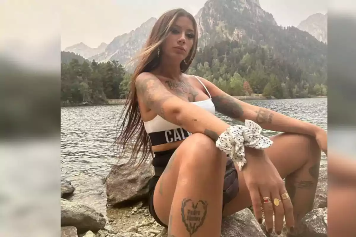 Mujer con tatuajes sentada junto a un lago rodeado de montañas y árboles Mujer con tatuajes sentada junto a un lago rodeado de montañas y árboles