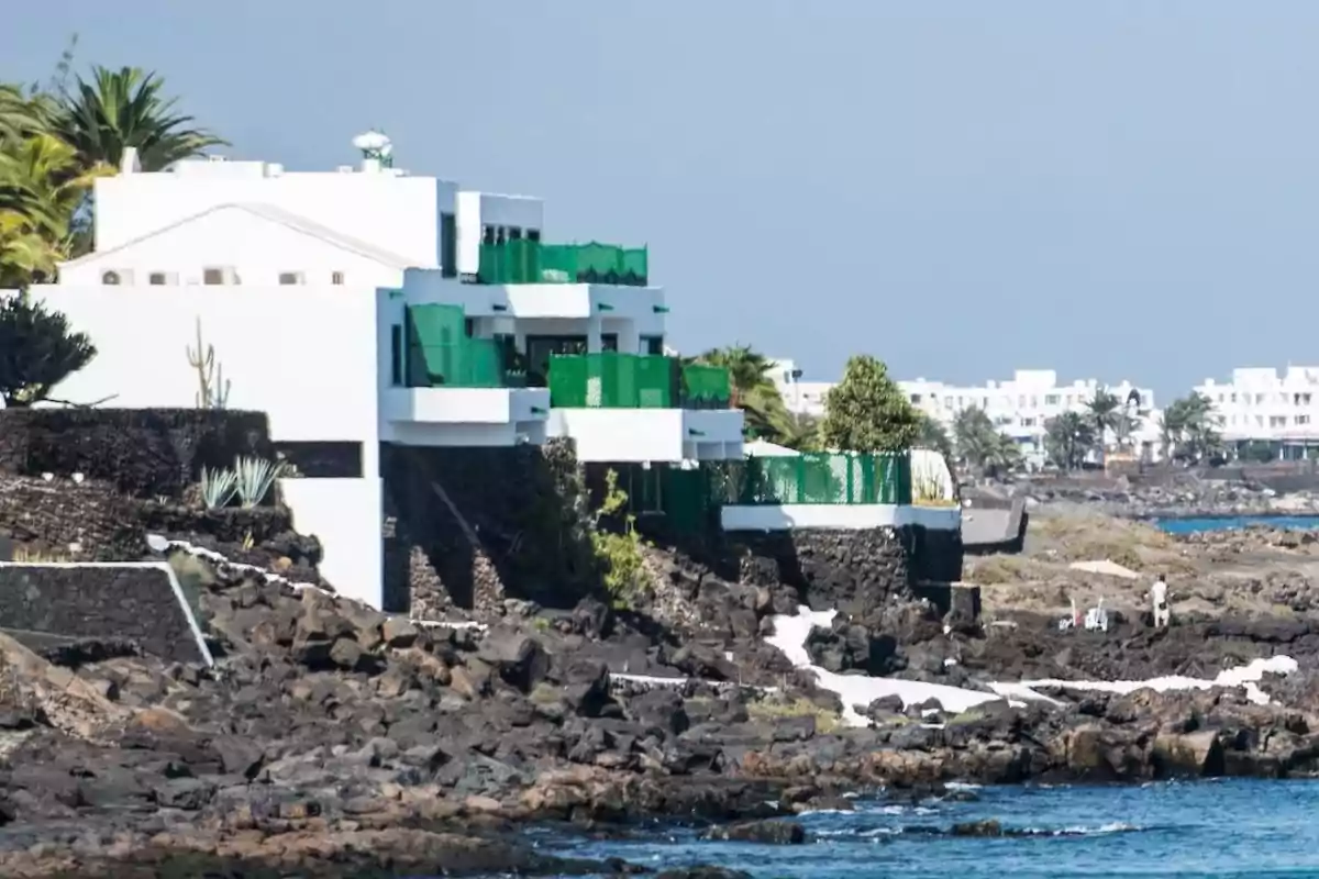 Casas blancas con detalles verdes construidas sobre rocas volcánicas junto al mar en una zona costera Casas blancas con detalles verdes construidas sobre rocas volcánicas junto al mar en una zona costera