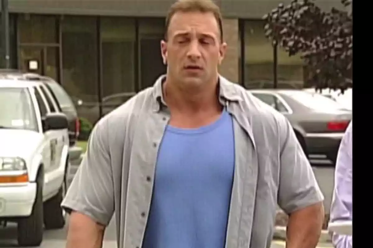 Hombre musculoso con camiseta azul y camisa gris caminando en un estacionamiento Hombre musculoso con camiseta azul y camisa gris caminando en un estacionamiento