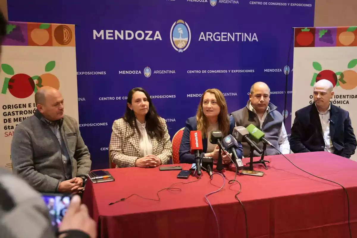 Cinco personas sentadas detrás de una mesa con micrófonos en una conferencia de prensa en Mendoza Argentina con carteles sobre gastronomía a los costados