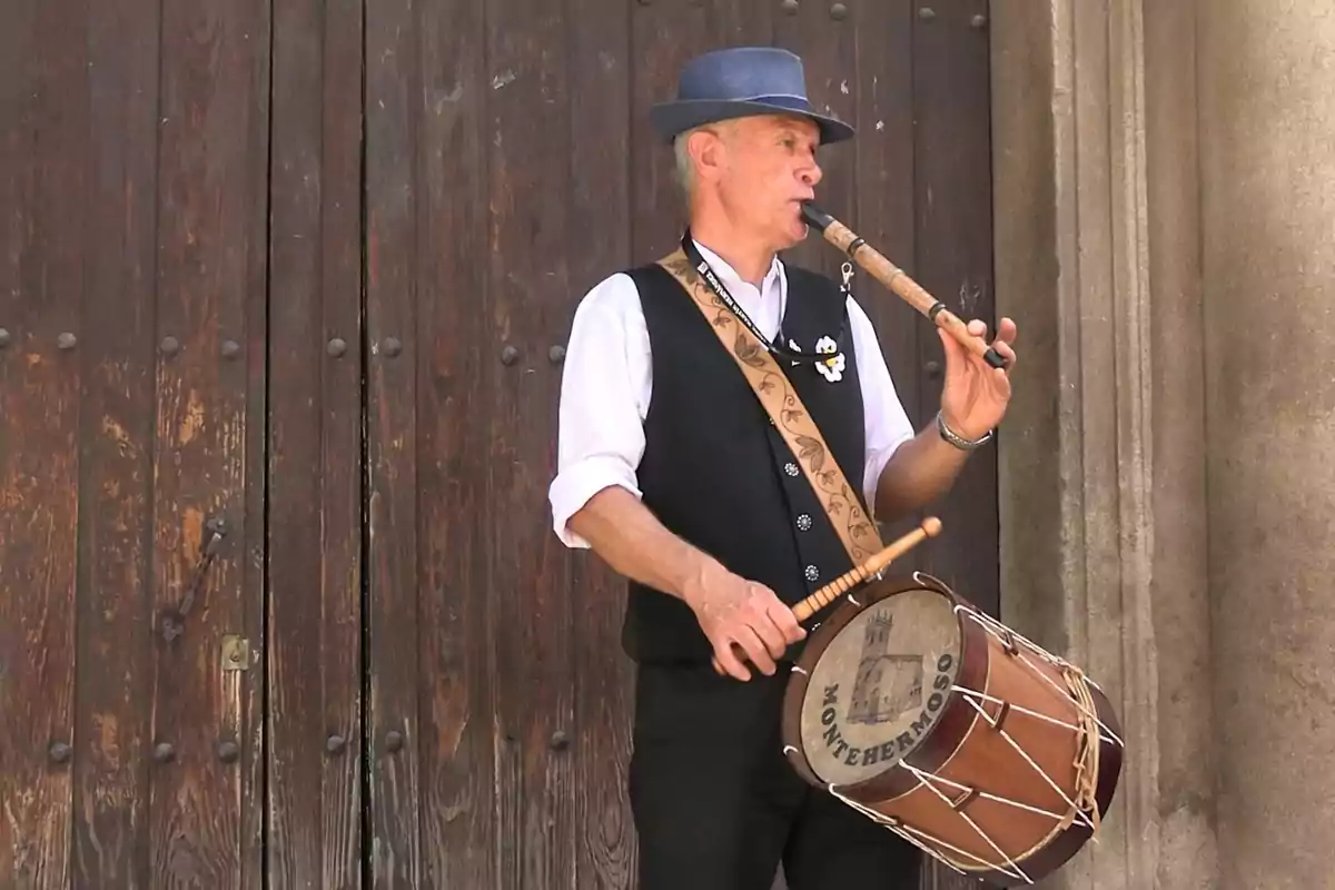 Hombre tocando una flauta y un tambor tradicional frente a una puerta de madera Hombre tocando una flauta y un tambor tradicional frente a una puerta de madera
